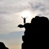 Persona celebrando en la cima de una roca, simbolizando la superación de obstáculos y el éxito personal, mentalidad ganadora