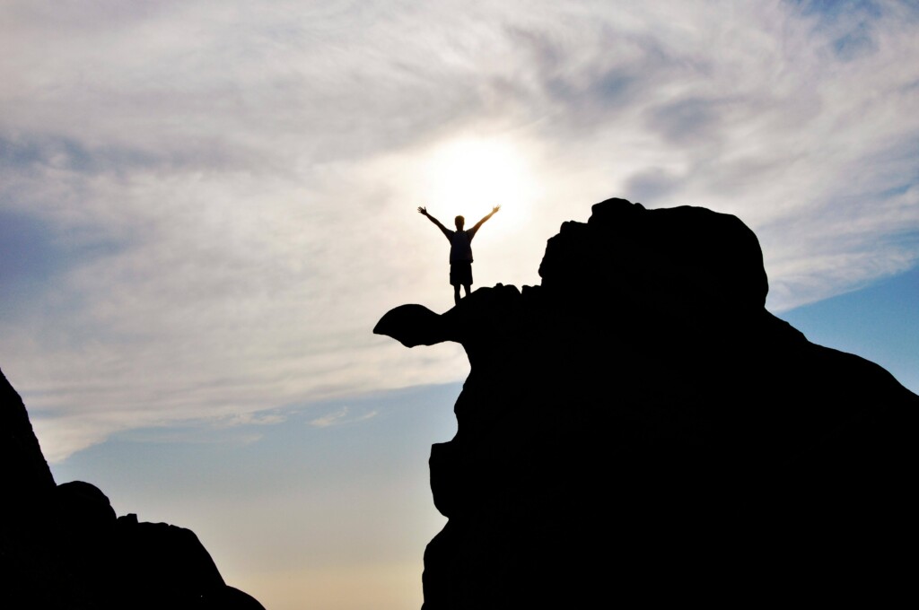 Persona celebrando en la cima de una roca, simbolizando la superación de obstáculos y el éxito personal, mentalidad ganadora